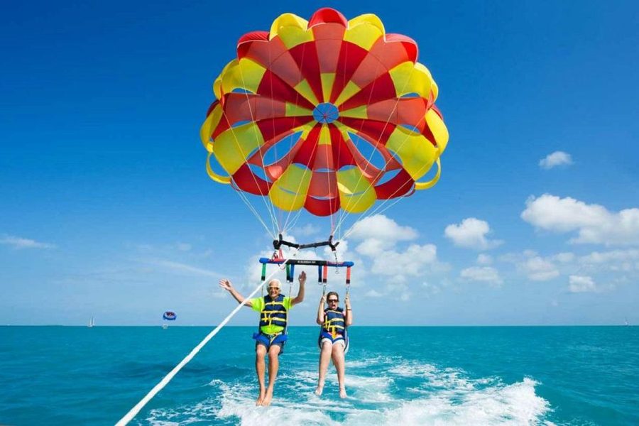 Two people in life jackets parasailing beneath a red and yellow parachute above turquoise sea