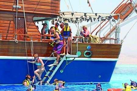 Guests in life vests and snorkelers at the boarding ladder of the Pirates I sailing boat off Hurghada