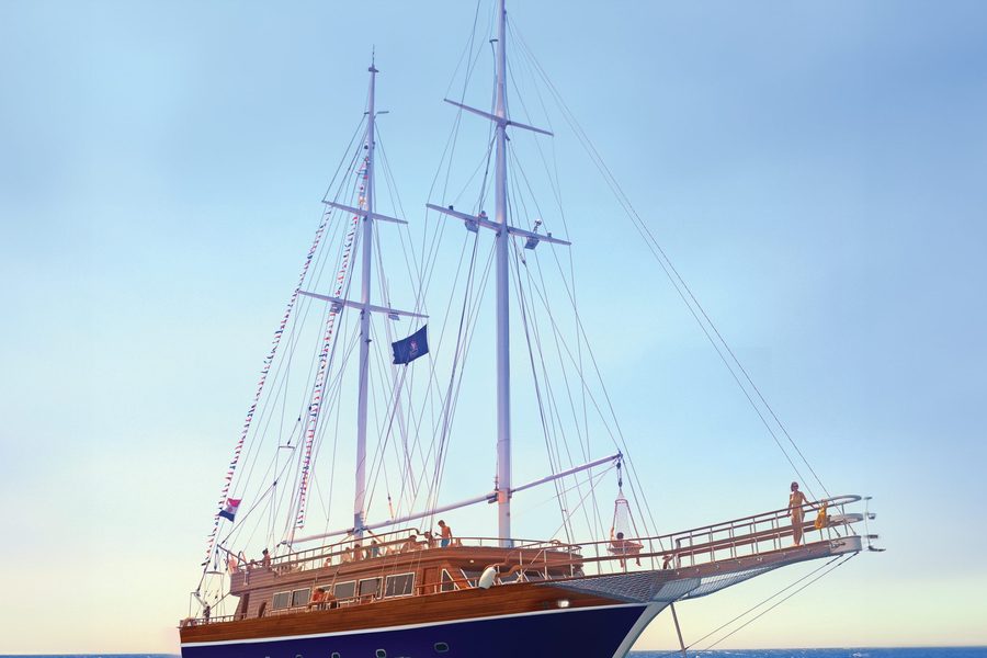 A two-masted wooden sailing boat with guests on deck, out at sea