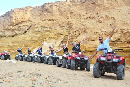 Group of quad bike riders raising their arms in a line in front of a sandstone cliff near Marsa Alam