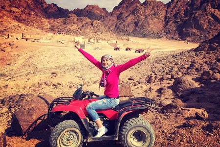 Tourist with arms raised on a red quad bike in a rocky desert valley near Hurghada
