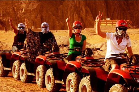 Four riders on red quad bikes in a row, flashing peace signs, during a desert quad safari near Hurghada