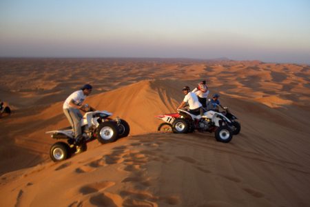 Quad bike riders on a red desert dune in warm evening light