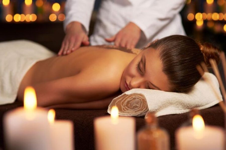 Therapist giving a relaxing back massage to a woman lying on a spa table among candles