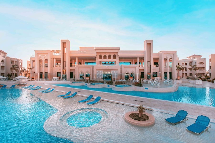 Hôtel de villégiature à Hurghada, doté d'une grande piscine, de transats bleus et de bâtiments roses de style mauresque