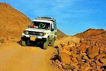 White 4x4 safari jeep with a roof rack driving along a rocky desert track between brown mountains