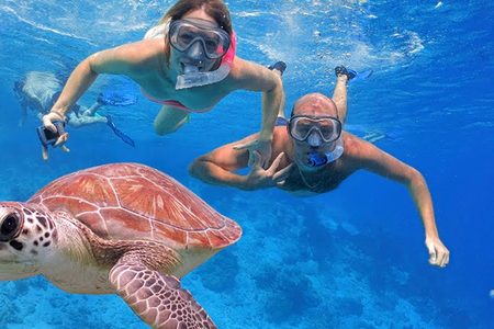 Two snorkelers with masks swimming alongside a sea turtle in deep blue water