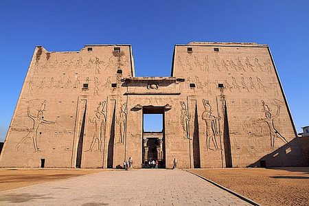Massive entrance pylon of the Temple of Horus at Edfu, carved with giant reliefs, under a deep blue sky