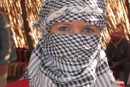 Tourist wrapped in a black and white desert scarf with only blue eyes showing, inside a reed-walled tent