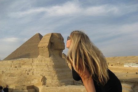 Tourist leaning in to kiss the Great Sphinx in a playful pose, with a pyramid behind at Giza