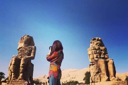 Tourist in a colorful jacket photographing the two Colossi of Memnon under a deep blue sky