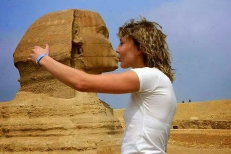 Tourist in a white T-shirt playfully posing as if kissing the face of the Great Sphinx at Giza