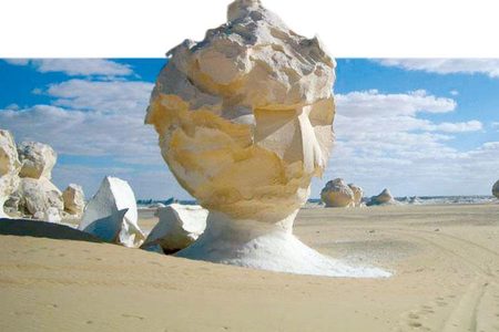 Lone white chalk rock formation on pale desert sand under a blue sky with clouds in the White Desert