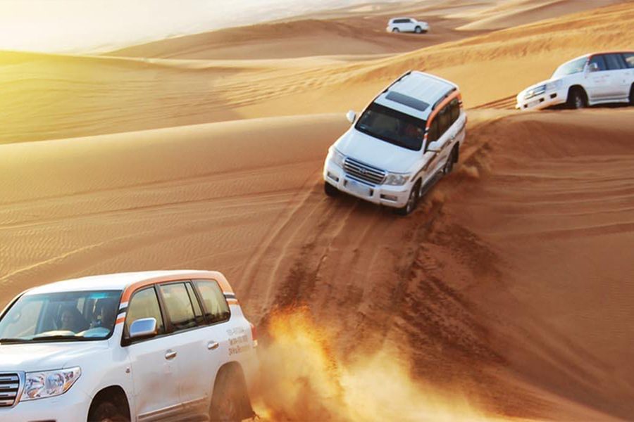 White 4x4 vehicles driving over desert dunes