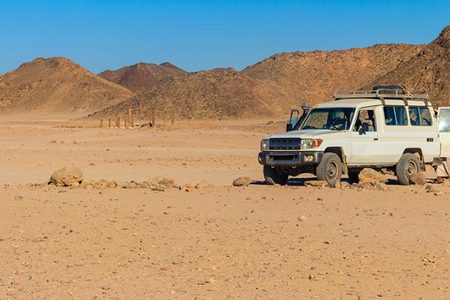 White safari jeep parked on stony desert ground below brown rocky hills during a desert safari near Hurghada