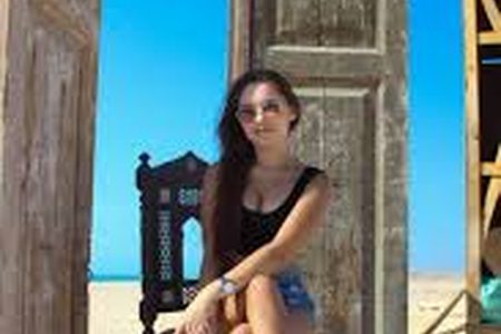 Woman posing on an ornate wooden chair in front of old carved wooden doors on a sandy beach