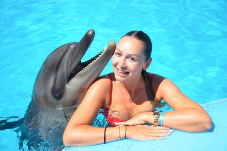 Smiling woman posing with a dolphin at the edge of a bright blue pool on a swim with dolphins in Hurghada