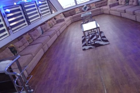 Spacious yacht lounge with a long beige sofa along the windows, wooden floor, glass tables and blue LED lighting