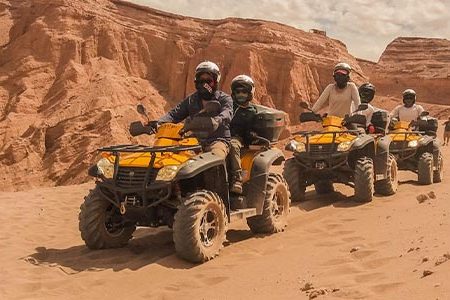 Group of helmeted riders on yellow quad bikes below red sandstone cliffs in the desert