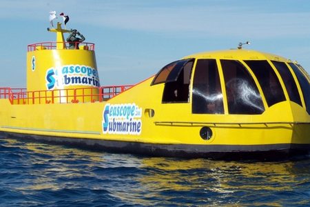 Yellow Seascope Submarine boat with a lookout figure holding binoculars on its red-railed tower under a blue sky